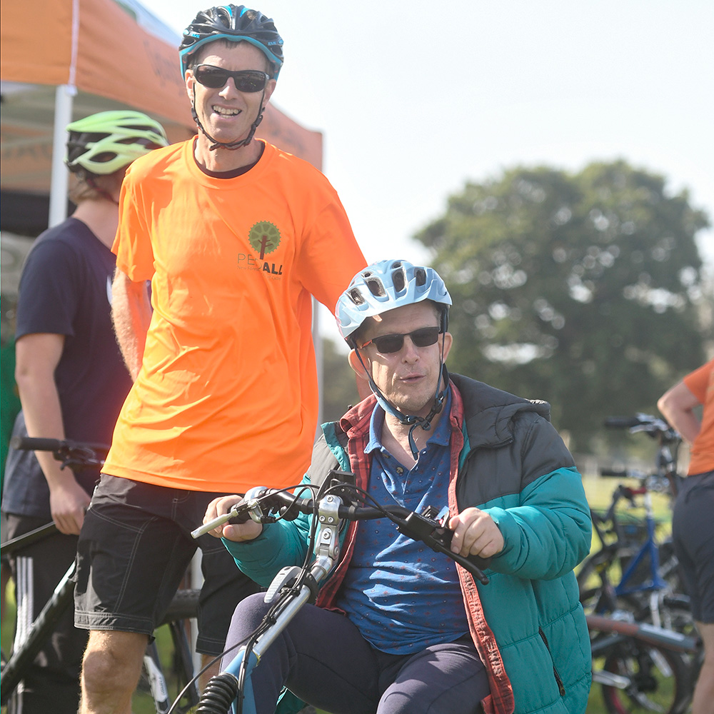 A PEDALL volunteer with a cyclist on an adaptive bike