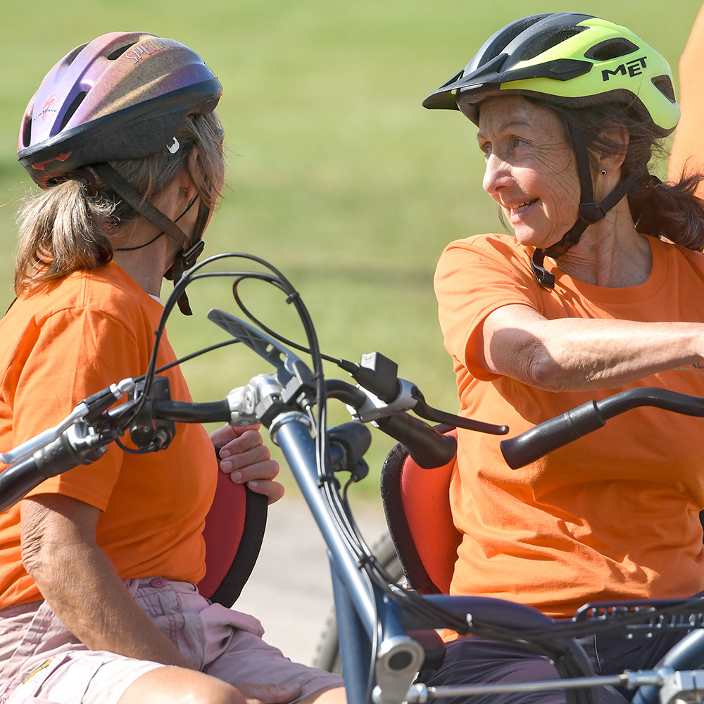 Two PEDALL volunteers on a tandem bike smiling and having a discussion