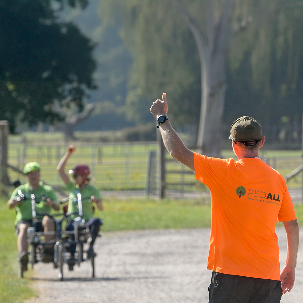 A PEDALL volunteer giving the thumbs up to two cyclists who are giving the thumbs up in return